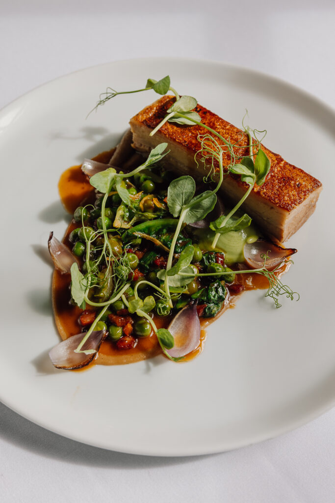 A plate of pork belly, jus and greens